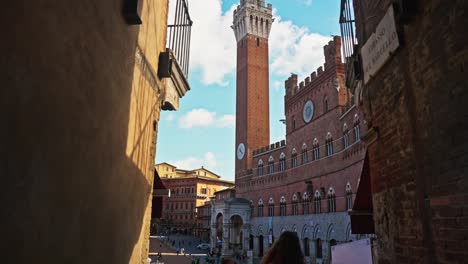 Walking-towards-the-Piazza-del-Campo-with-the-Tower-of-Mangia-in-the-background,-Siena,-Italy