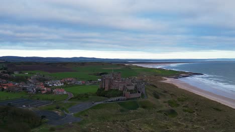 Slow-aerial-pullback-reveal-of-Bamburgh-Castle,-Northumberland-and-stunning-surrounding-landscape