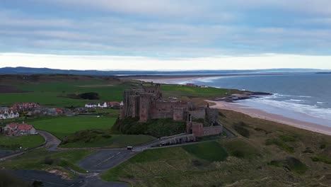 Closeup-ascending-orbit-of-Bamburgh-Castle-showing-the-the-beauty-of-the-sea,-beach-and-surrounding-islands