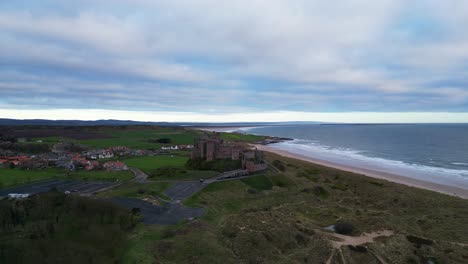 Aerial-rise-and-tilt-view-of-Bamburgh-Castle,-the-sandy-beach,-the-North-Sea-and-to-Lindisfarne-Island-beyond