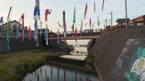 Carp-Fish-Flags-"Koinobori"-Along-River-in-Rural-Japanese-Town,-Push-Shot