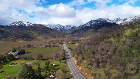 Fast-aerial-glide-above-Napa-Valley-vineyards-following-a-road-to-snow-white-mountains