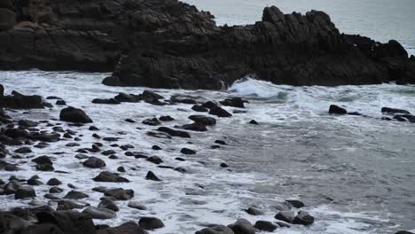 Sea-waves-loosing-their-power-and-crashing-into-rocks-at-the-beach,-captured-during-daytime,-untouched-nature-concept