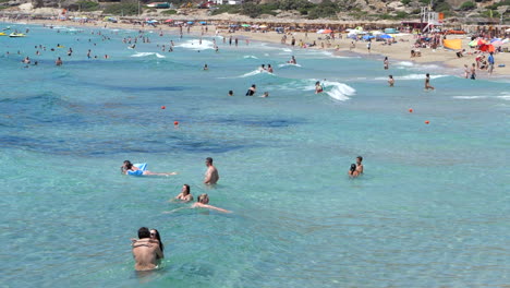 Sunny-day-on-Falasarna-beach,-couple-embracing-in-foreground