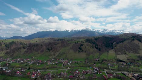 Drone-View-Of-The-Majestic-Bucegi-Mountains,-With-Patches-Of-Snow,-Pittoresque-Mountain-Village-And-Green-Fields,-Romania,-Transilvania,-Moieciu,-Rucar,-Bran
