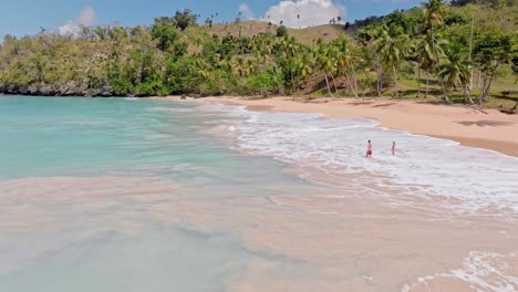 Two-travelers-frolic-in-waves-of-idyllic-Playa-Colorada,-Caribbean