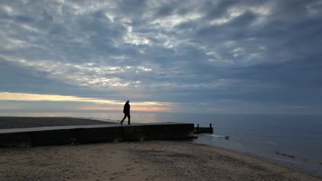 Slow-motion-wide-shot-of-man-walking-to-end-of-jetty-at-dusk-on-Fleetwood-Beach-Lancashire-UK