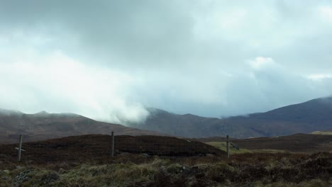 Static-shot-of-a-misty-mountain-range-behind-a-fence-on-a-peatland-moor-covered-in-heather