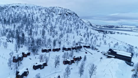 Snow-covered-hotel-cabins-at-base-of-white-tree-lined-mountain