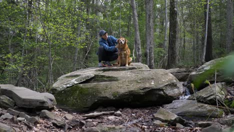 A-young-woman-and-her-dog-stop-on-large-rock-during-hiking-trail-in-upstate-new-york