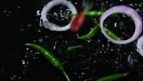 Close-up-shot-top-view-of-green-chili-pepper-and-sliced-onion-ring-falling-and-bouncing-in-the-water
