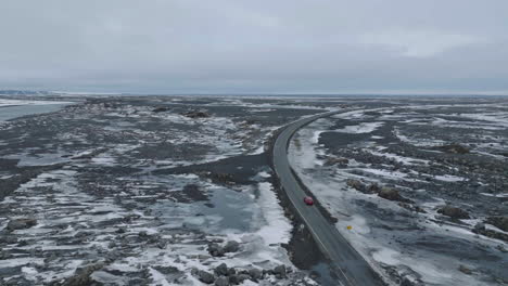 Drone-Shot-of-Car-Moving-on-Wet-Road-in-Landscape-of-Iceland-During-Late-Winter-Season