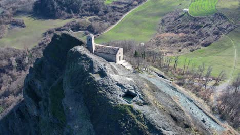 Aerial-footage-of-Pietra-Perduca,-volcanic-rock,-church-set-at-top-stone-immersed-in-countryside-landscape,-cultivated-land-in-Val-Trebbia-Bobbio,-Emilia-Romagna,-Italy