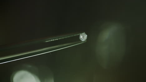 Close-up-shot-of-a-real-diamond-getting-held-by-a-pair-of-tweezers-with-a-blurry-bokeh-background-and-shiny-reflected-light-LOG