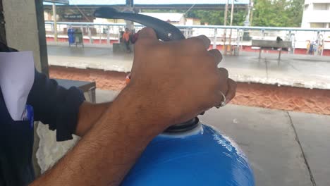 Un-Hombre-Colocando-El-Cabezal-De-Retrolavado-Del-Recipiente-Ro-Con-La-Mano-En-El-Tanque-Azul-De-La-Máquina-Expendedora-De-Agua-Ro-En-La-Plataforma-De-La-Estación-De-Tren