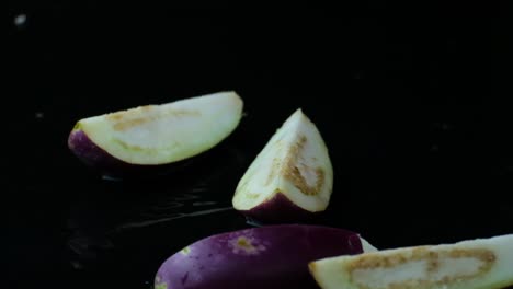 in-quarters-sliced-aubergines-falling-down-into-clean-puddle-with-black-studio-background