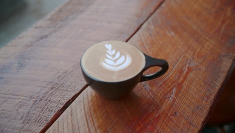 Handheld-parallax-of-latte-art-in-black-teacup-with-white-leaves-at-cafe