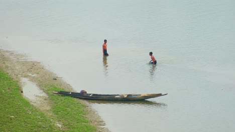 Asian-kids-bathing-in-river-by-traditional-canoe,-rural-Bangladesh