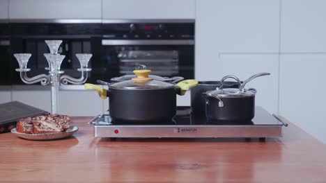 Hand-Stellt-Kochtöpfe-Auf-Einen-Geräumigen-Keramikherd,-Der-Auf-Der-Küchenarbeitsplatte-Platziert-Ist