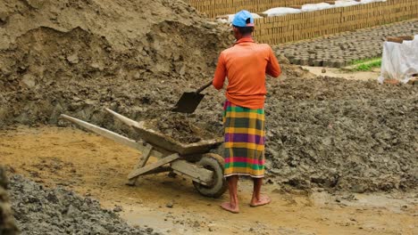 Asian-worker-fills-wheelbarrow-with-clay-in-brick-factory