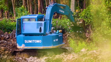 Blue-excavator-moving-soil-near-lush-green-forest