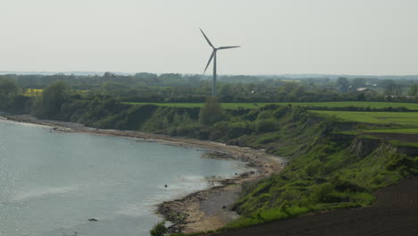 Dynamische-Küstenwindkraftanlage:-Schnelle-Rotation-In-Der-Nähe-Von-Klippen-Und-Wasser-Auf-Einer-Grünen-Wiese-In-Dänemark