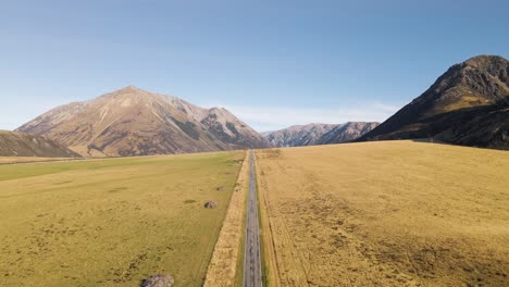 Straight-road-surrounded-by-rugged-mountains-and-golden-plains