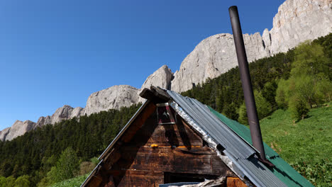 Tall-granite-cliffs-and-pine-tree-forest-behind-wooden-sheet-metal-shack,-kavkaz-mountain