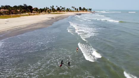 Aerial-push-in-view-of-waves-on-shoreline-and-tourists-swimming-at-Cape-Point,-Bakau---The-Gambia