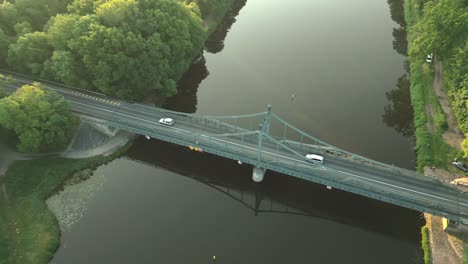 Luftaufnahme-Der-Reich-Verzierten-Stahlbrücke-über-Den-Fluss-Mit-Vorbeifahrenden-Autos-In-Der-Morgensonne