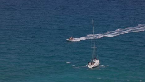 Sailboat-sailing-and-speedboat-navigating-leaving-white-wake-on-blue-sea-surface