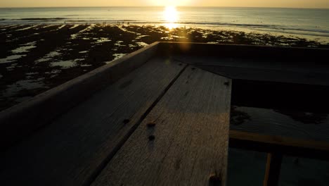 Dolly-forward-shot-on-a-wooden-handrail-overlooking-Suluban-Beach-at-sunset-and-low-tide-with-the-reef-visible-and-people-walking