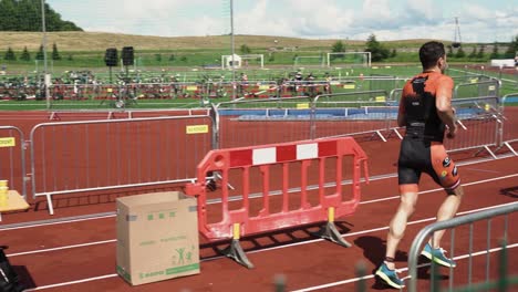 Male-triathlete-finishes-third-leg-running-along-track-past-water-station