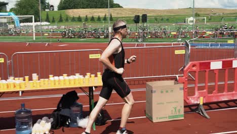 Triathlon-runner-passing-by-water-tables-in-local-stadium,-slow-motion-view