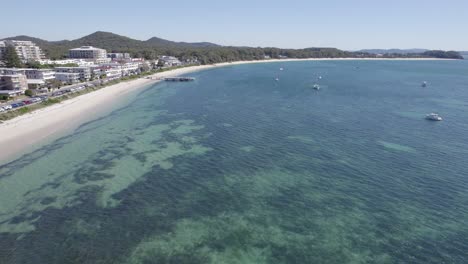 Flying-Over-The-Clear-Water-Of-Shoal-Bay-With-Sailing-Boats-In-Summer-In-NSW,-Australia