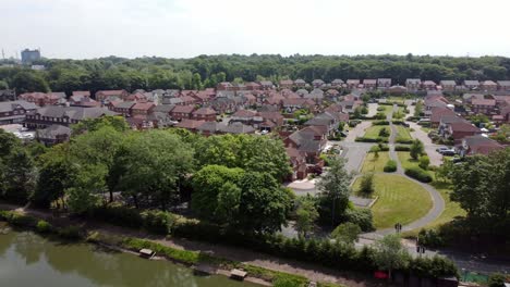 Woodland-lakeside-red-brick-British-townhouse-development-neighbourhood-aerial-view-panning-across-detached-property