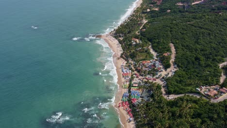 Vista-Superior-De-La-Famosa-Playa-Tropical-De-Coqueirinhos-En-Paraiba,-Brasil-Con-Coloridas-Sombrillas-De-Playa-Para-Turistas,-Palmeras,-Arena-Dorada-Y-Agua-Turquesa
