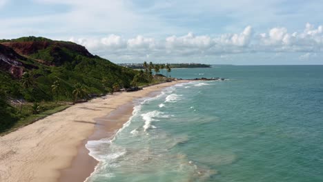 Beautiful-aerial-drone-dolly-in-shot-of-the-tropical-coastline-of-Paraiba,-Brazil-near-the-famous-destination-Coqueirinhos-beach-with-palm-trees,-tall-cliffs,-golden-sand-and-clear-crystal-ocean-water