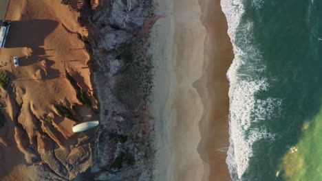Aerial-drone-bird's-eye-top-view-following-a-paraglider-flying-over-the-Cliffs-of-Cacimbinhas-in-Pipa,-Brazil-Rio-Grande-do-Norte-as-small-waves-crash-into-the-beach-on-a-warm-summer-day