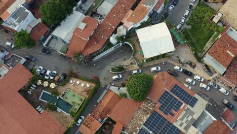 Rising-aerial-drone-shot-looking-down-at-the-small-cobblestone-road-of-the-center-of-the-famous-tropical-beach-town-of-Pipa,-Brazil-in-Rio-Grande-do-Norte-with-people-and-cars-passing-down-the-road