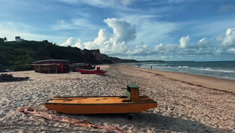Beautiful-handheld-landscape-shot-of-a-small-yellow-boat-docked-on-the-tropical-Love-beach-in-Paraiba,-Brazil-with-golden-sand,-turquoise-water,-and-blue-cloudy-skies-on-a-warm-sunny-summer-day
