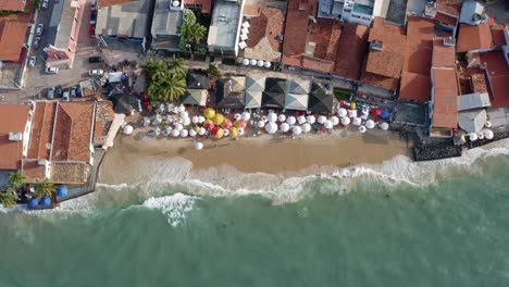 Aerial-drone-birds-eye-shot-of-the-beautiful-tropical-famous-Pipa-beach-during-high-tide-with-tourists-playing-in-the-water-and-enjoying-the-shade-under-colorful-umbrellas-during-a-warm-summer-evening