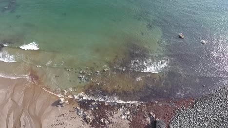 Aerial-birdseye-view-of-waves-gently-breaking-towards-the-rocky-beach