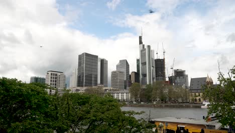 Frankfurt-Skyline-View-From-Across-River-Main-Over-Tree-Line-With-Light-Wind-Blowing-And-Birds-Flying-Past