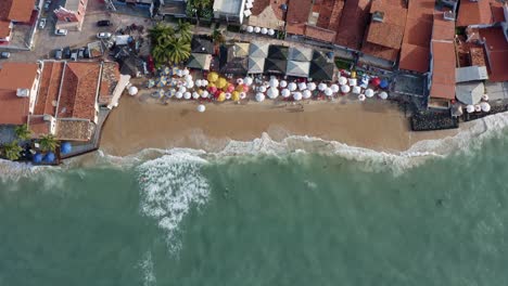 Aerial-drone-birds-eye-shot-of-the-beautiful-tropical-famous-Pipa-beach-during-high-tide-with-tourists-playing-in-the-water-and-enjoying-the-shade-under-colorful-umbrellas-on-a-summer-evening