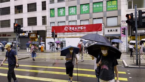 Asiatische-Menschen-überqueren-Den-Zebrastreifen-In-Wan-Chai-Mit-Regenschirmen-An-Einem-Regnerischen-Tag,-Hongkong