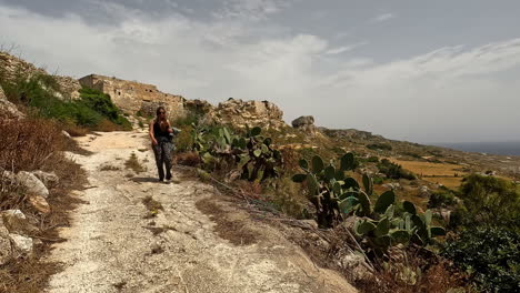 Woman-walking-through-arid-and-rocky-terrain-on-a-dry-path-with-cacti-and-vegetation