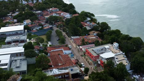 Rising-aerial-drone-shot-following-a-tourist-jeep-driving-down-the-main-road-of-the-famous-tropical-tourist-beach-town-of-Pipa,-Brazil-in-Rio-Grande-do-Norte