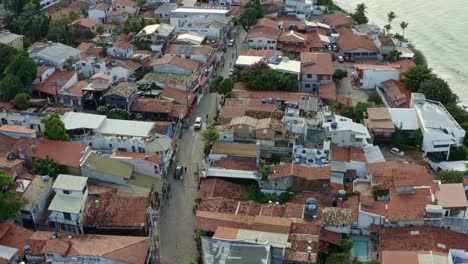 Rotating-aerial-drone-shot-looking-down-at-the-small-cobblestone-road-of-the-center-of-the-famous-tropical-beach-town-of-Pipa,-Brazil-in-Rio-Grande-do-Norte-with-people-and-cars-passing-down-the-road