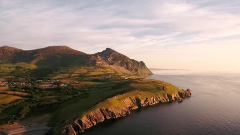 Aerial-view-right-to-left-of-Mountain-range-Yr-Eifl-at-Trefor-with-granite-quarry-and-view-of-Trefor-Village-with-blue-skies-on-a-summers-day-across-the-Irish-Sea-on-the-Llyn-Peninsula-in-North-Wales